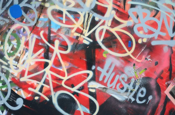 Close-up fragment of a graffiti drawing applied to the wall by aerosol paint. The wall is spoiled by a multitude of colorful signatures and tags from street artists and hooligans
