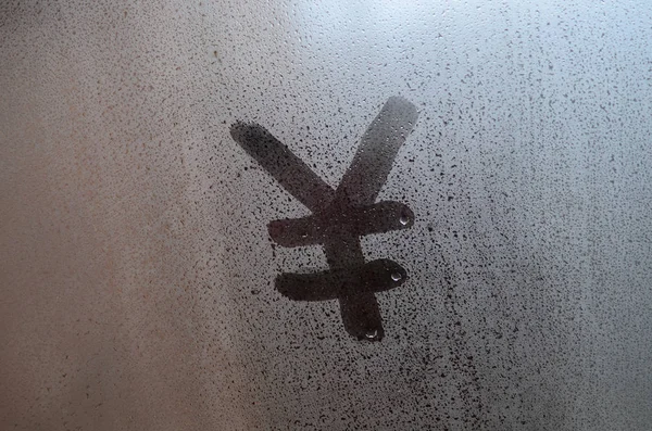 Chinese Yen Symbol is written with a finger on the surface of the misted glass