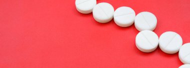 Birkaç beyaz tablet parlak kırmızı bir arka plan yüzeyinde yatıyor. Tıbbi ve ilaç konularında arkaplan resmi