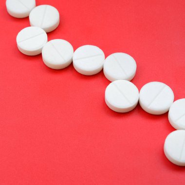 Birkaç beyaz tablet parlak kırmızı bir arka plan yüzeyinde yatıyor. Tıbbi ve ilaç konularında arkaplan resmi