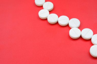 Birkaç beyaz tablet parlak kırmızı bir arka plan yüzeyinde yatıyor. Tıbbi ve ilaç konularında arkaplan resmi