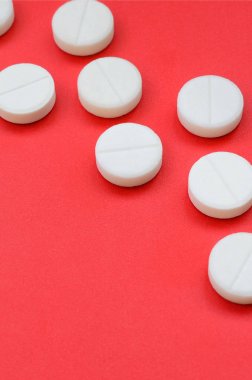 Birkaç beyaz tablet parlak kırmızı bir arka plan yüzeyinde yatıyor. Tıbbi ve ilaç konularında arkaplan resmi