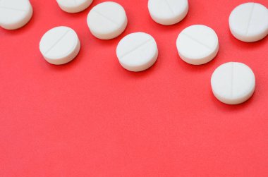 Birkaç beyaz tablet parlak kırmızı bir arka plan yüzeyinde yatıyor. Tıbbi ve ilaç konularında arkaplan resmi