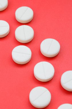 Birkaç beyaz tablet parlak kırmızı bir arka plan yüzeyinde yatıyor. Tıbbi ve ilaç konularında arkaplan resmi