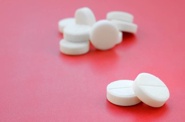 Birkaç beyaz tablet parlak kırmızı bir arka plan yüzeyinde yatıyor. Tıbbi ve ilaç konularında arkaplan resmi