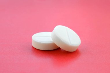 Birkaç beyaz tablet parlak kırmızı bir arka plan yüzeyinde yatıyor. Tıbbi ve ilaç konularında arkaplan resmi