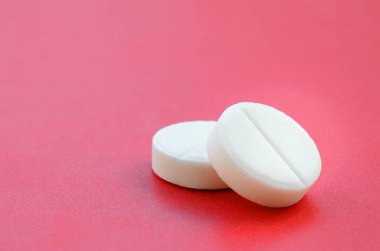 Birkaç beyaz tablet parlak kırmızı bir arka plan yüzeyinde yatıyor. Tıbbi ve ilaç konularında arkaplan resmi