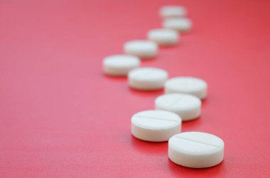 Birkaç beyaz tablet parlak kırmızı bir arka plan yüzeyinde yatıyor. Tıbbi ve ilaç konularında arkaplan resmi