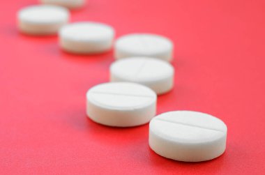 Birkaç beyaz tablet parlak kırmızı bir arka plan yüzeyinde yatıyor. Tıbbi ve ilaç konularında arkaplan resmi