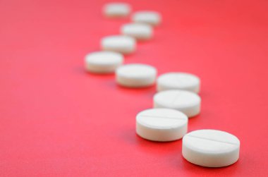 Birkaç beyaz tablet parlak kırmızı bir arka plan yüzeyinde yatıyor. Tıbbi ve ilaç konularında arkaplan resmi