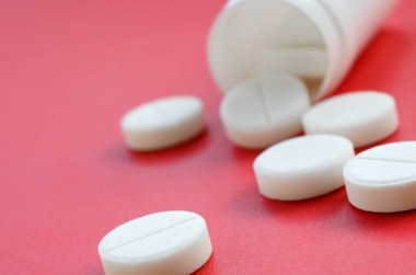 Birkaç beyaz tabletler kırmızı yüzeyinde plastik kavanozdan düşmek. İlaç ve tıbbi konularda arka plan görüntüsü