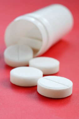 Birkaç beyaz tabletler kırmızı yüzeyinde plastik kavanozdan düşmek. İlaç ve tıbbi konularda arka plan görüntüsü