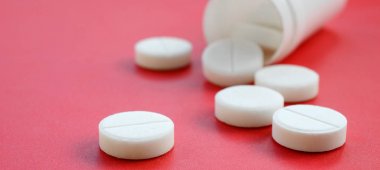 Birkaç beyaz tabletler kırmızı yüzeyinde plastik kavanozdan düşmek. İlaç ve tıbbi konularda arka plan görüntüsü