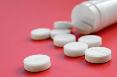 Birkaç beyaz tabletler kırmızı yüzeyinde plastik kavanozdan düşmek. İlaç ve tıbbi konularda arka plan görüntüsü