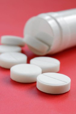 Birkaç beyaz tabletler kırmızı yüzeyinde plastik kavanozdan düşmek. İlaç ve tıbbi konularda arka plan görüntüsü