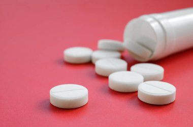 Birkaç beyaz tabletler kırmızı yüzeyinde plastik kavanozdan düşmek. İlaç ve tıbbi konularda arka plan görüntüsü