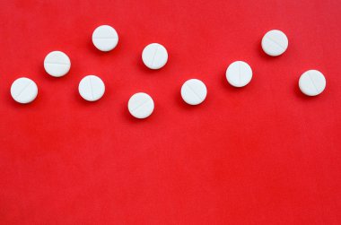 Birkaç beyaz tablet parlak kırmızı bir arka plan yüzeyinde yatıyor. Tıbbi ve ilaç konularında arkaplan resmi