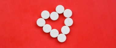 Birkaç beyaz tabletler parlak kırmızı bir arka plan bir kalp şeklinde yalan. Tıp ve eczacılık konularda arka plan görüntüsü