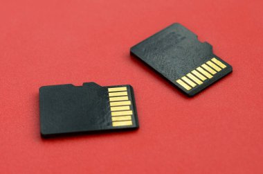 Two small micro SD memory cards lie on a red background. A small and compact data and information store clipart