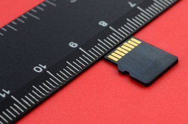 Küçük micro Sd hafıza kartı yalan siyah bir cetvel yanında kırmızı bir arka plan üzerinde. Küçük ve kompakt veri ve bilgi deposu