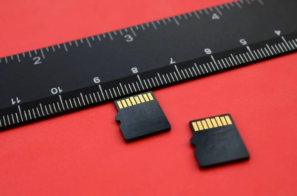 两个小的微型 存储卡位于黑色标尺旁边的红色背景上 小型和紧凑的数据和信息存储 — 图库照片