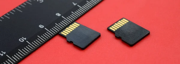 Two small micro SD memory cards lie on a red background next to a black ruler. A small and compact data and information store