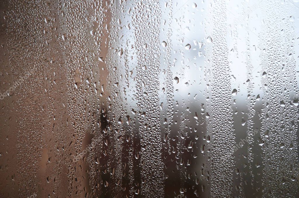 A photo of the glass surface of the window, covered with a multitude of droplets of various sizes. Background texture of a dense layer of condensate on glass