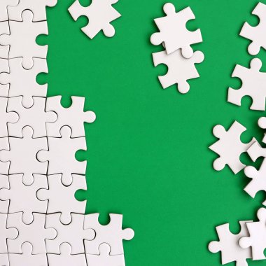 Katlanmış bir beyaz jigsaw puzzle ve bir yığın uncombed bulmaca öğeleri arka planı yeşil yüzey parçası. Metin için yer ile doku fotoğraf