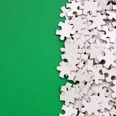 Bir yığın beyaz jigsaw puzzle uncombed unsurlarının bir yeşil yüzey arka plan üzerinde yatıyor. Metin kopyalama yeri olan doku fotoğraf
