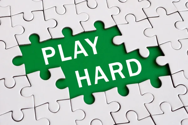 White jigsaw puzzle in assembled state with missing elements forming a green space with white inscription. Play hard