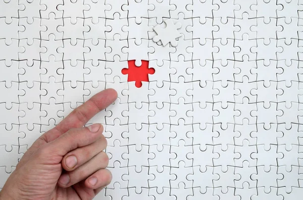 The texture of a white jigsaw puzzle in the assembled state with one missing element, forming a red space, pointed to by the finger of the male hand