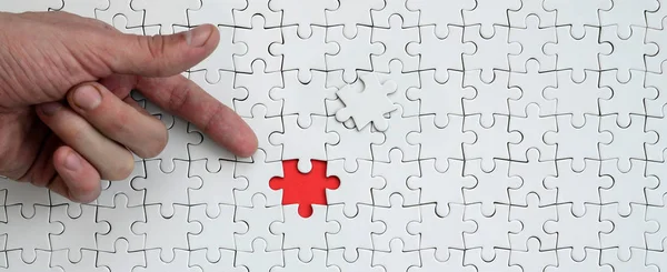The texture of a white jigsaw puzzle in the assembled state with one missing element, forming a red space, pointed to by the finger of the male hand