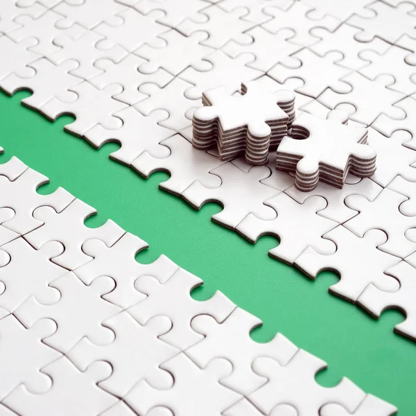 The green path is laid on the platform of a white folded jigsaw puzzle. The missing elements of the puzzle are stacked nearby. Texture image with space for text