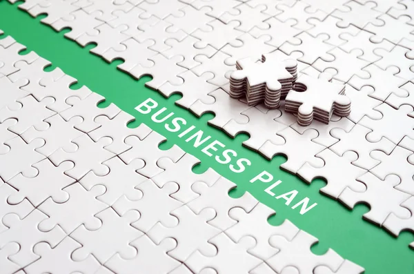 Business plan. The green path is laid on the platform of a white folded jigsaw puzzle. The missing elements of the puzzle are stacked nearby