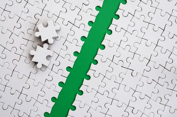 The green path is laid on the platform of a white folded jigsaw puzzle. The missing elements of the puzzle are stacked nearby. Texture image with space for text