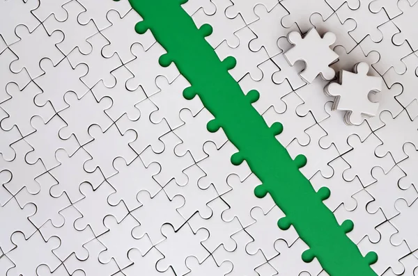 The green path is laid on the platform of a white folded jigsaw puzzle. The missing elements of the puzzle are stacked nearby. Texture image with space for text