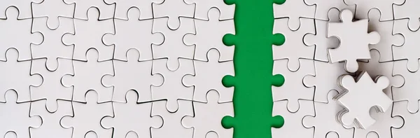 The green path is laid on the platform of a white folded jigsaw puzzle. The missing elements of the puzzle are stacked nearby. Texture image with space for text