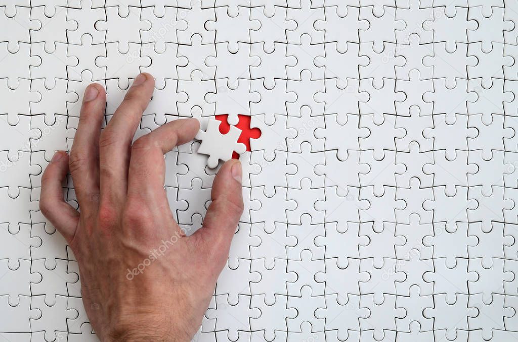 The texture of a white puzzle puzzle in the assembled state with one missing element that the male hand puts in