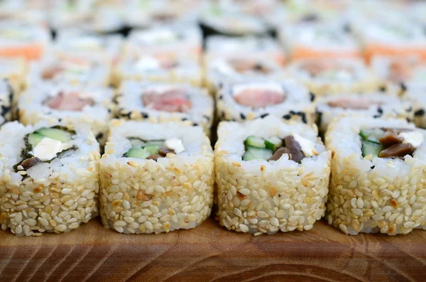 Close-up of a lot of sushi rolls with different fillings lie on a wooden surface. Macro shot of cooked classic Japanese food with a copy space