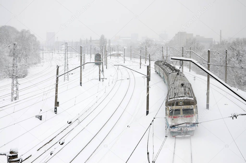 A long train of passenger cars is moving along the railway track. Railway landscape in winter after snowfall
