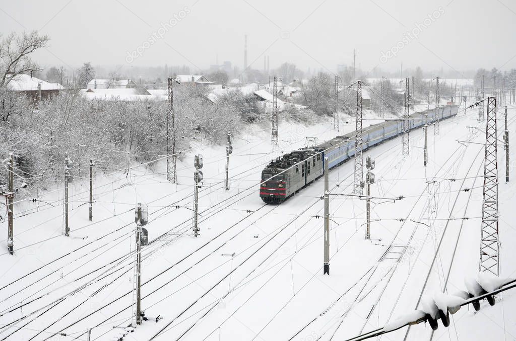 A long train of passenger cars is moving along the railway track. Railway landscape in winter after snowfall