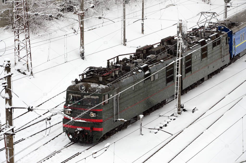 A long train of passenger cars is moving along the railway track. Railway landscape in winter after snowfall