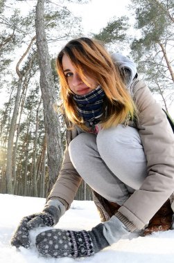 Kahverengi bir ceket genç ve neşeli beyaz kız kış aylarında karla kaplı bir ormandaki bir kartopu sculpts. Açık havada kar oyunlar. Balıkgözü fotoğraf