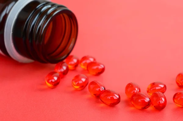 A lot of transparent red tablets were scattered from a small glass brown jar on a red surface