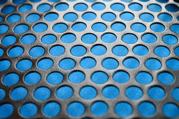 Black metal computer case panel mesh with holes on blue background. Abstract close up image