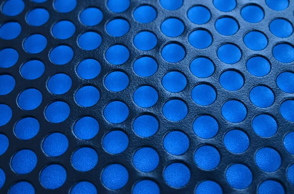 Black metal computer case panel mesh with holes on blue background. Abstract close up image