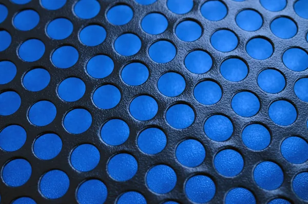 Black metal computer case panel mesh with holes on blue background. Abstract close up image