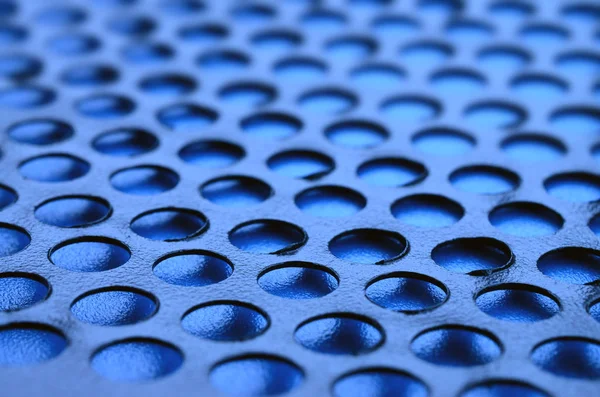 Black metal computer case panel mesh with holes on blue background. Abstract close up image