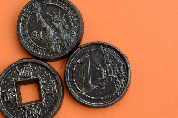 Three chocolate products in the form of Euro, USA and Japan coins lie on an orange plastic background. A model of cash coins in an edible form