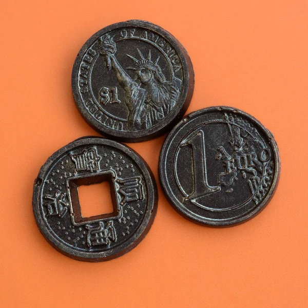 Three chocolate products in the form of Euro, USA and Japan coins lie on an orange plastic background. A model of cash coins in an edible form